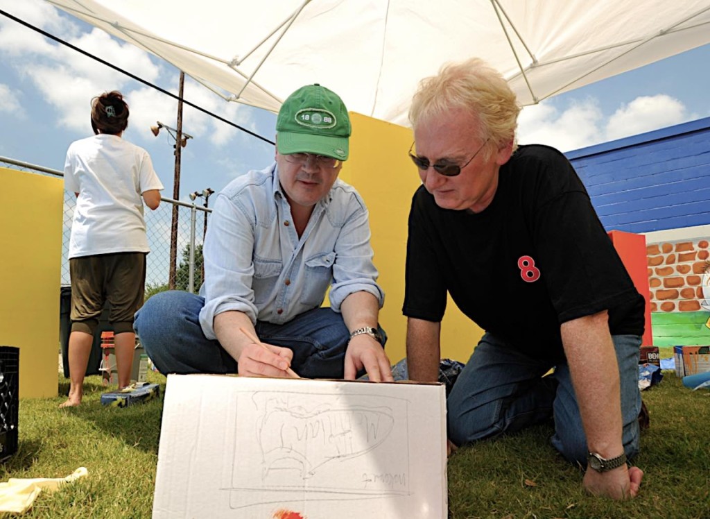 Two men squatting down and working on a box outside