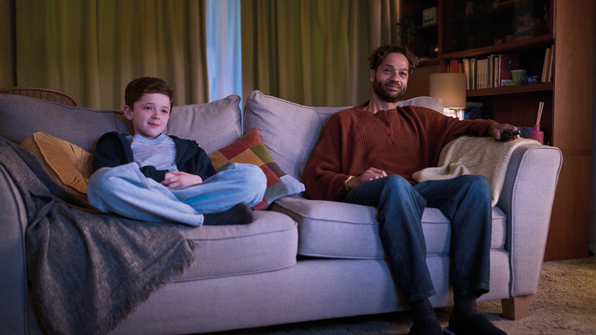 Young white boy and older black man on couch watching tv togther
