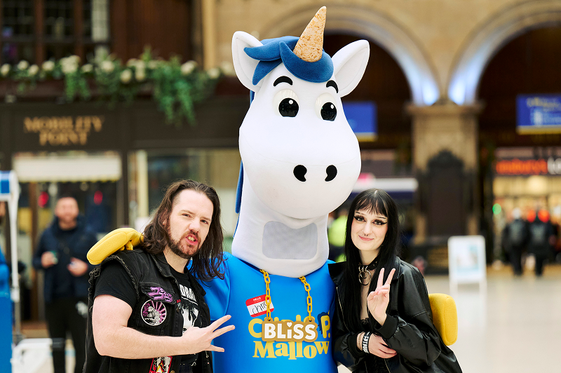 Two people on either side of a unicorn mascot