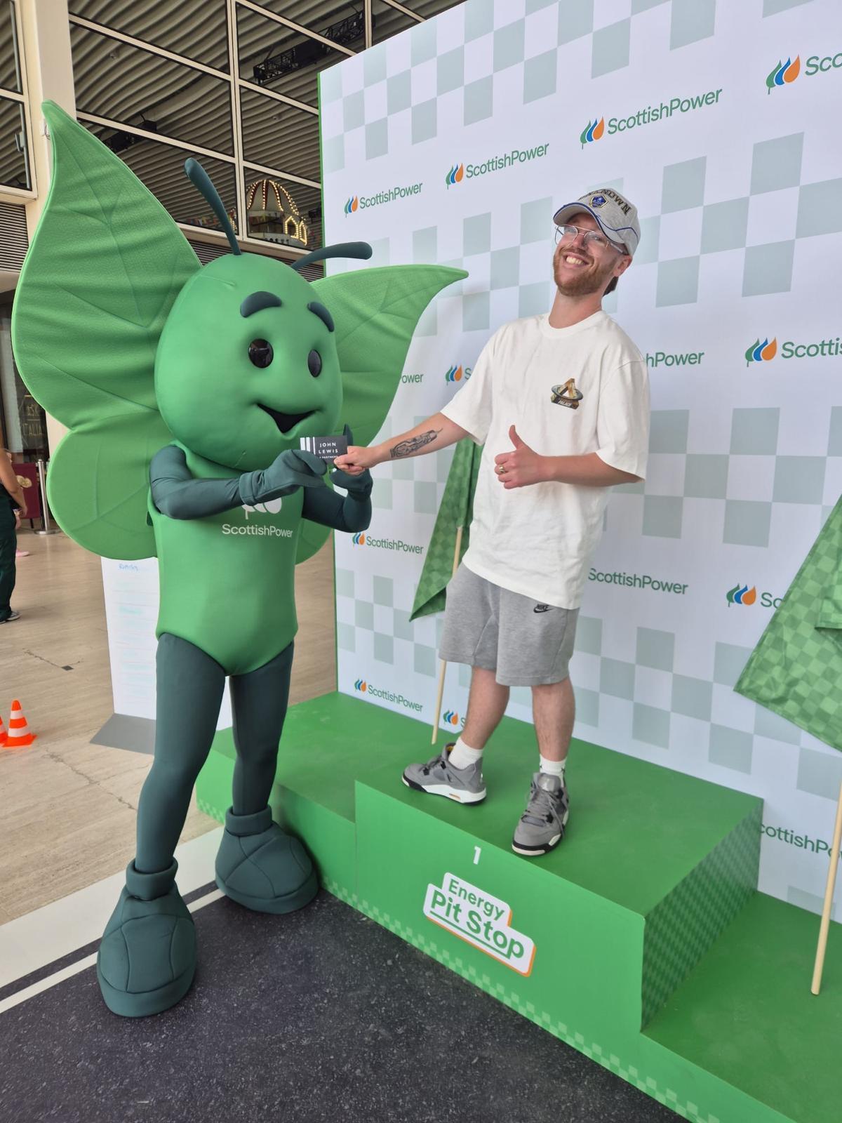 Man on podium being presented with item from Scottish Power mascot giant green butterfly